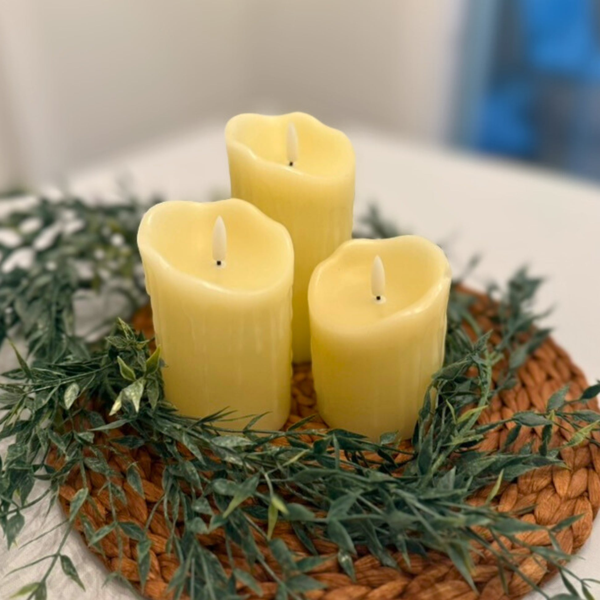 Three ivory pillar candles on a woven mat with greenery for rent - Picture Perfect Rentals