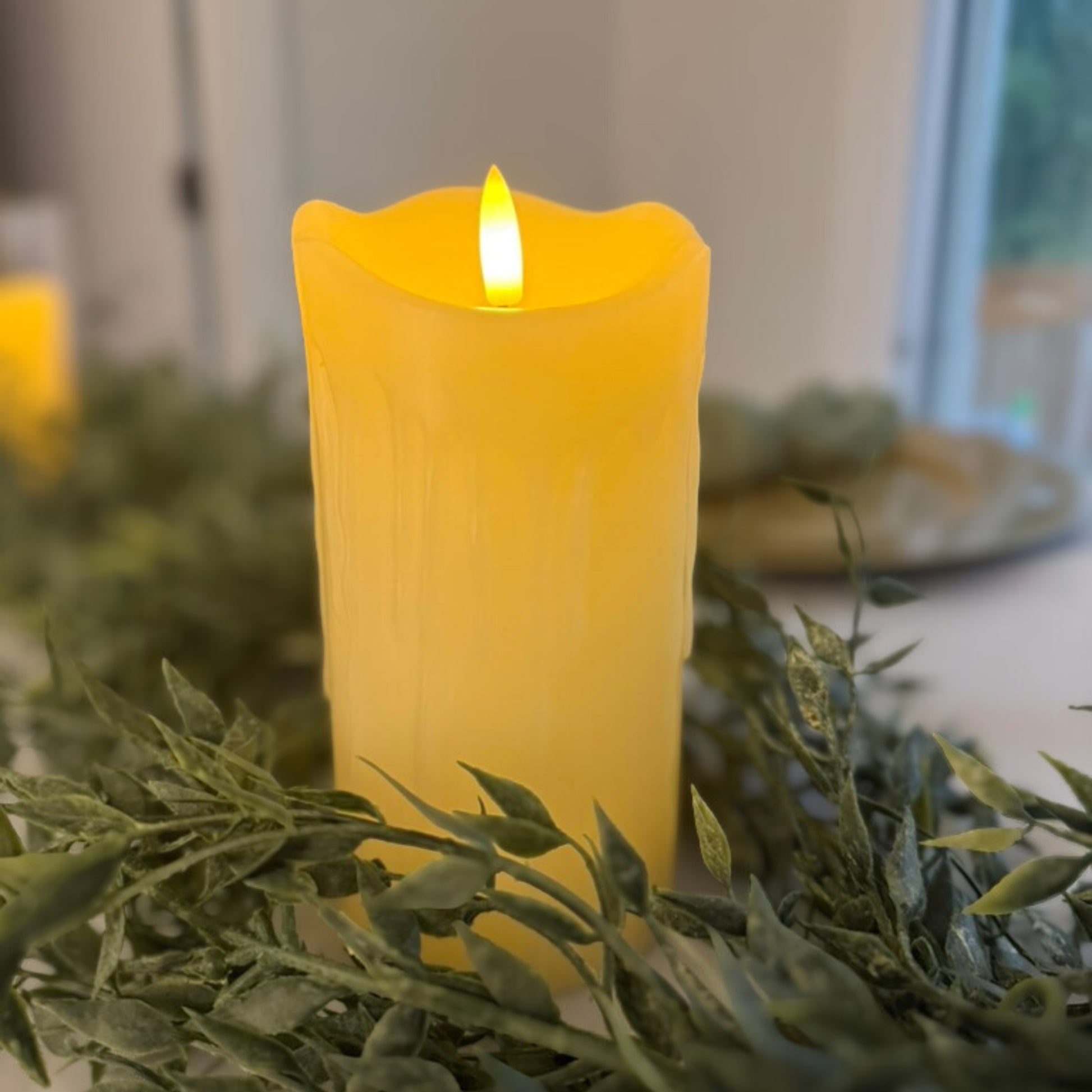 Ivory flameless pillar candle with a flame on green foliage - Picture Perfect Rentals