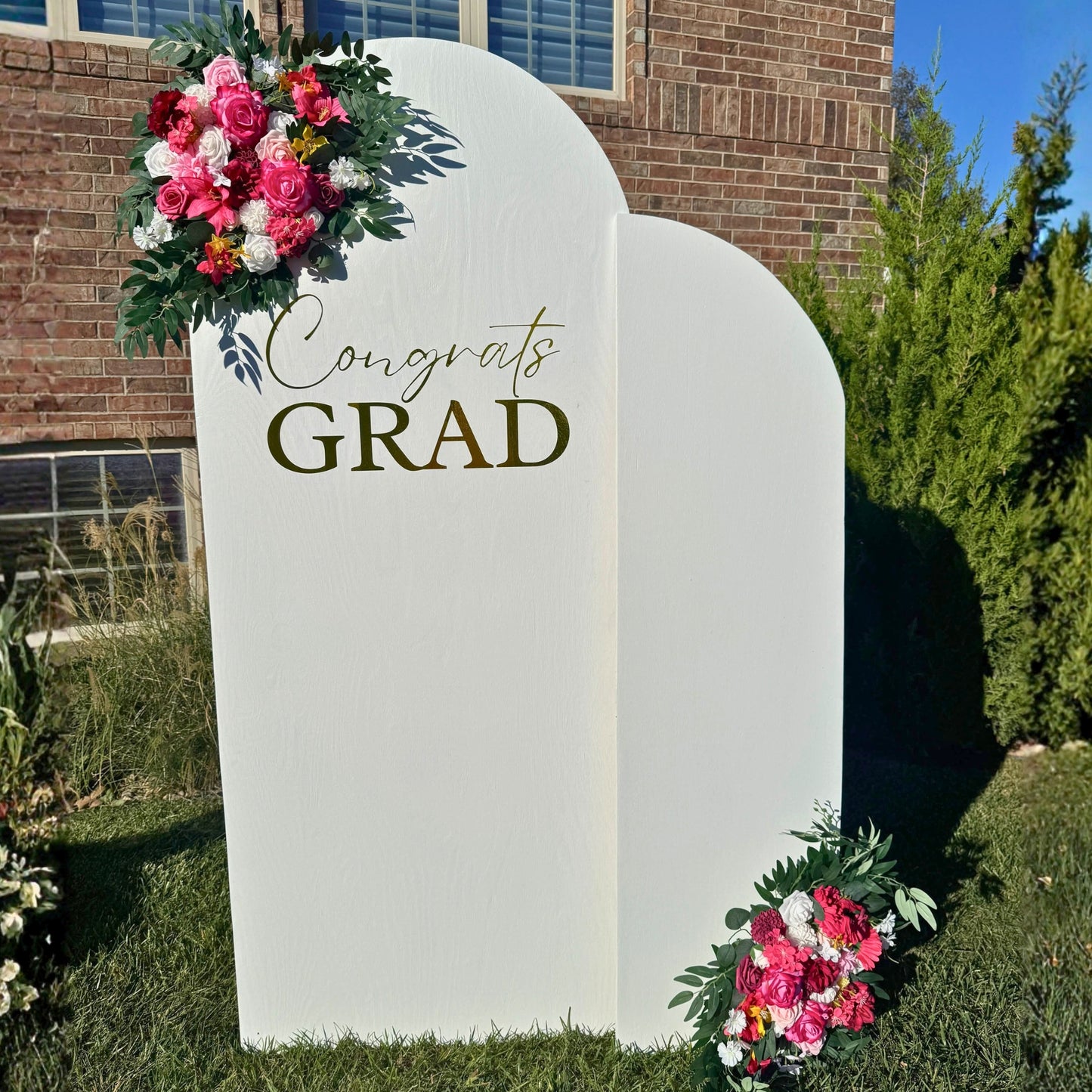 Graduation-themed decorative stand with flowers and 'Congrats GRAD' text in front of a brick building.